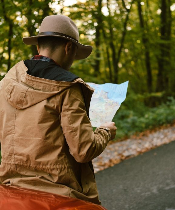 Traveler man with hat looking map near car in autumn forest